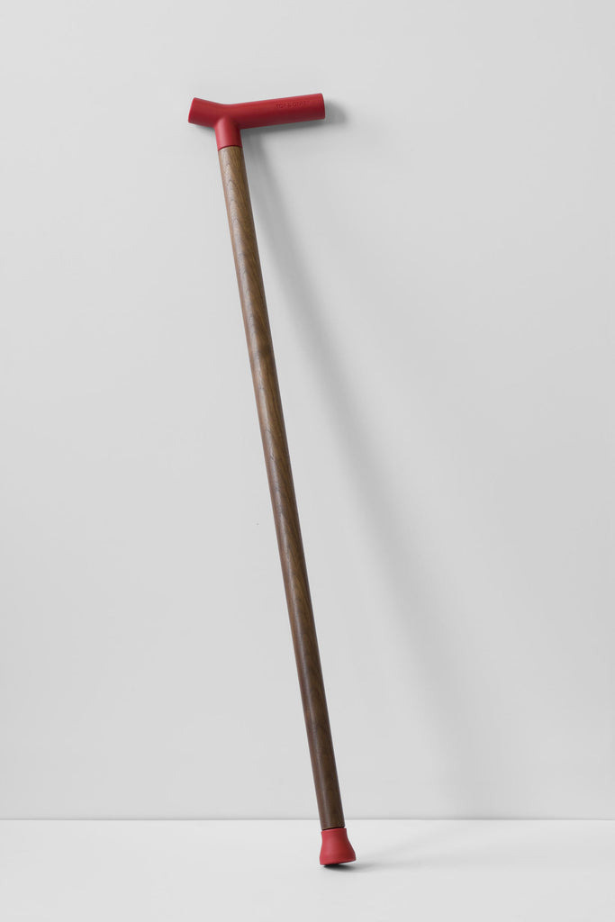 Fashionable walnut and red rubber walking cane leaning against white wall